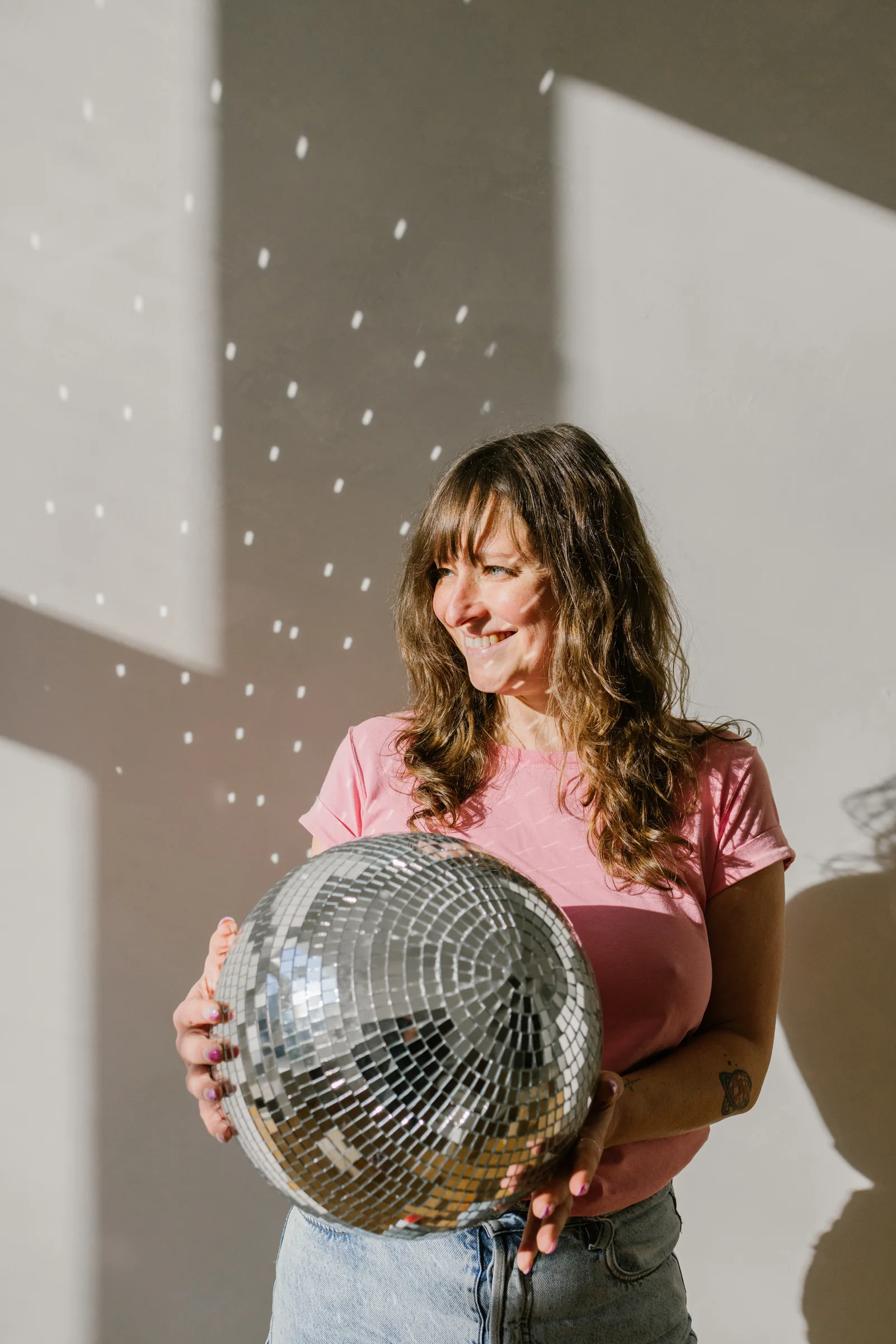 Amélie Beerens laughing, a disco ball in her hands, in a studio.