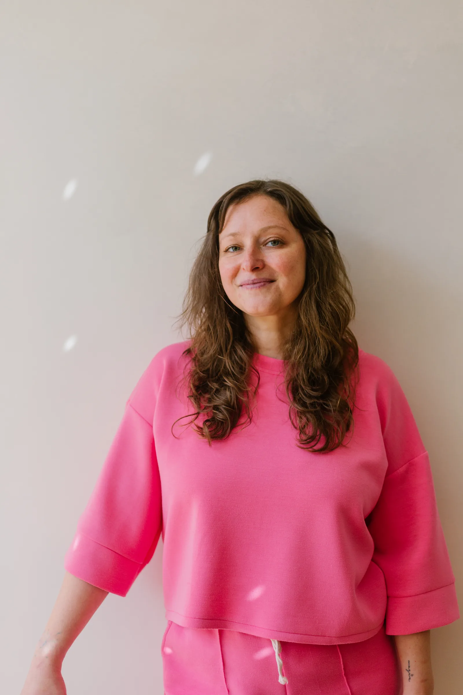 Amélie Beerens in a pink top against a pale wall, smiling at the camera.
