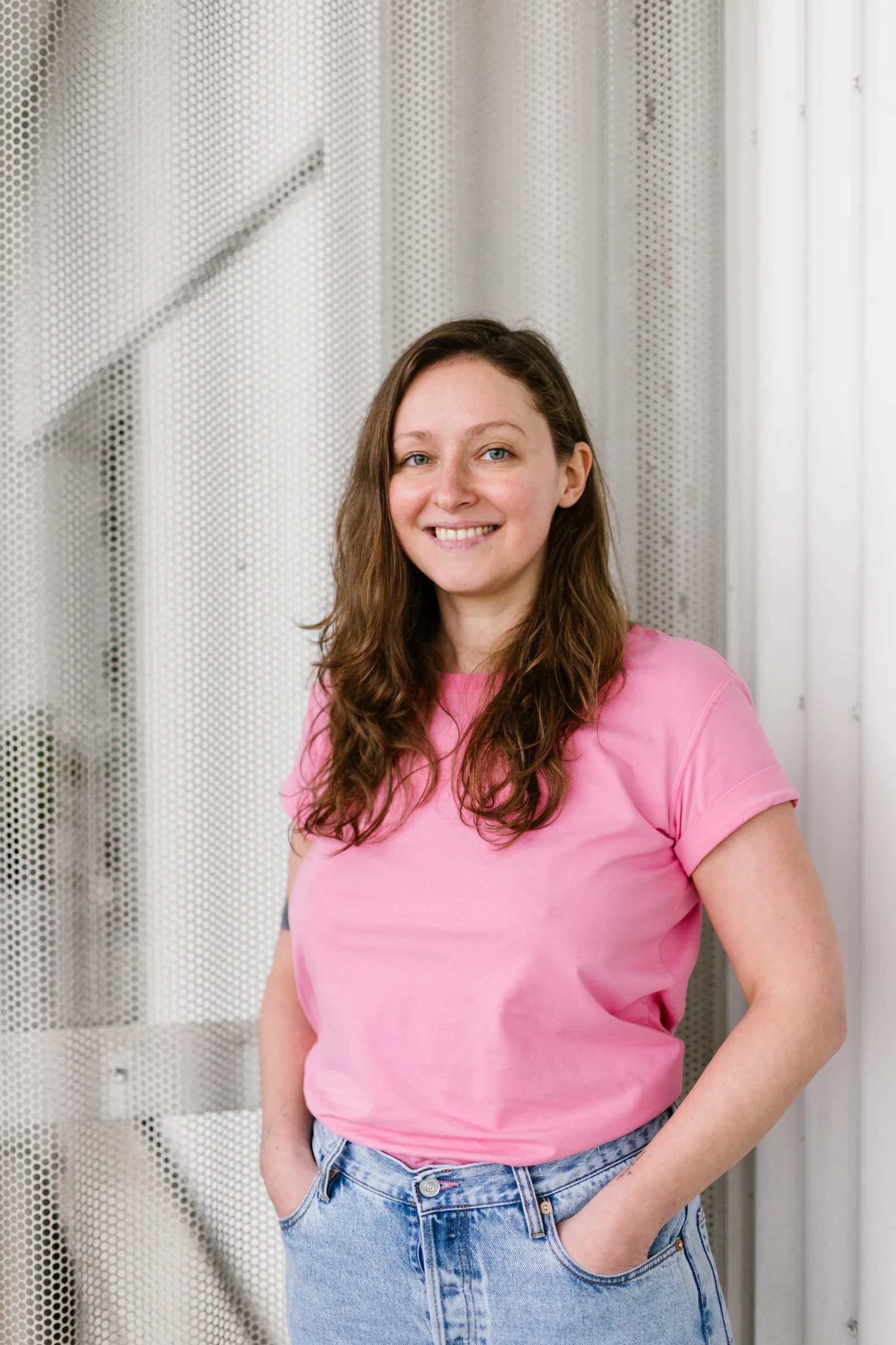 Amélie Beerens standing with her hands in her pockets, smiling at the camera, in front of a mesh wall.