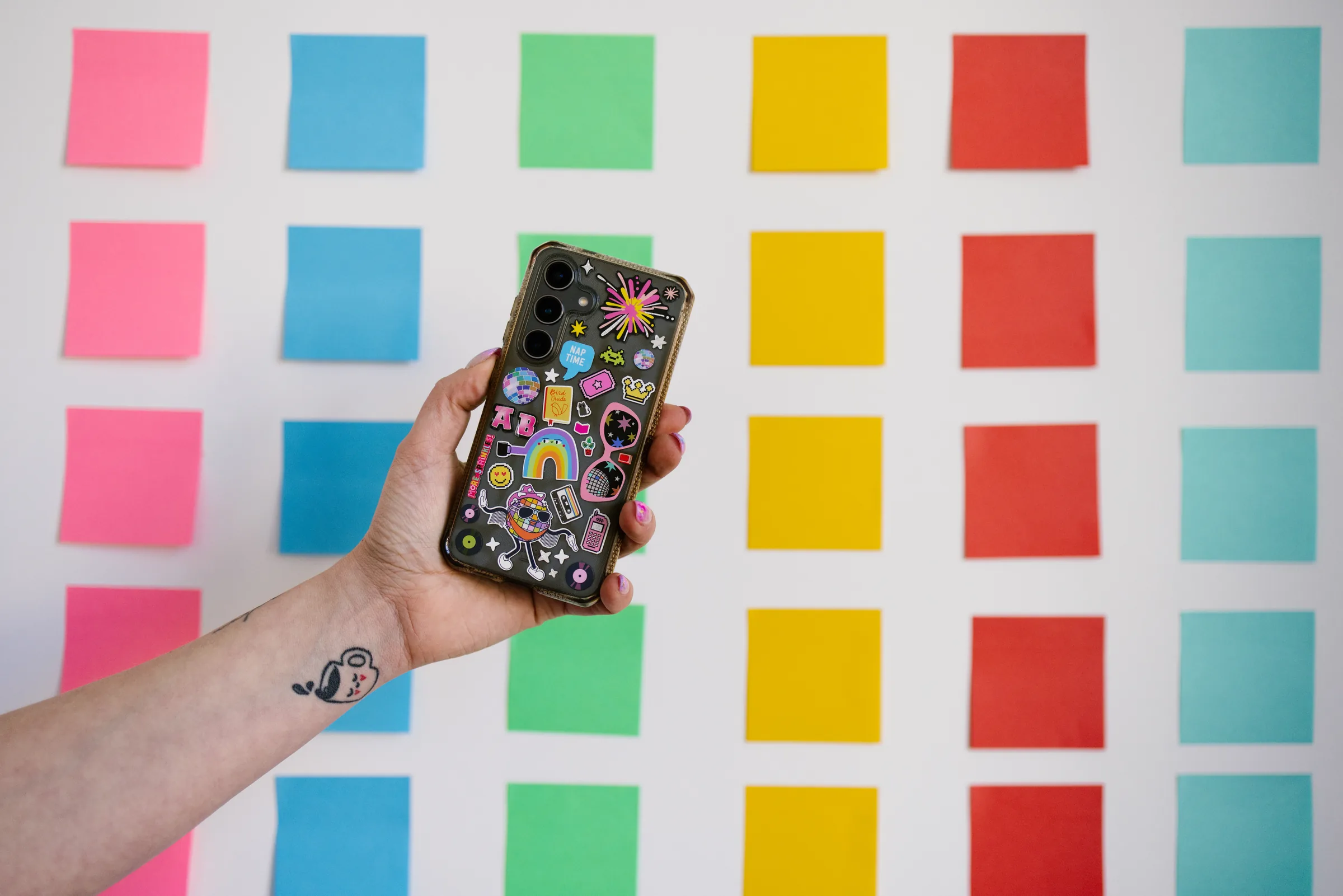 Amélie Beerens holding up a phone covered in stickers in front of a wall of coloured sticky notes.