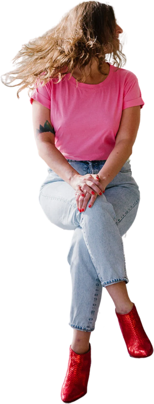 Amélie Beerens in a pink T-shirt, jeans and red boots, sitting with her hands on her knee, hair blown to the side.